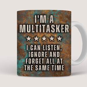 May include: A white ceramic coffee mug with a rusty brown and teal design. The mug features the text "I'M A MULTITASKER" with five stars and the text "I CAN LISTEN, IGNORE AND FORGET ALL AT THE SAME TIME".