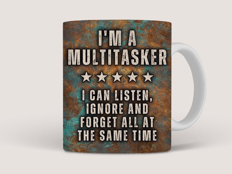 May include: A white ceramic coffee mug with a rusty brown and teal design. The mug features the text "I'M A MULTITASKER" with five stars and the text "I CAN LISTEN, IGNORE AND FORGET ALL AT THE SAME TIME".