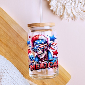 May include: A glass tumbler with a bamboo lid and a straw. The tumbler has a colorful graphic of a skeleton wearing sunglasses and a bandana with the word "MERICA" printed on it.