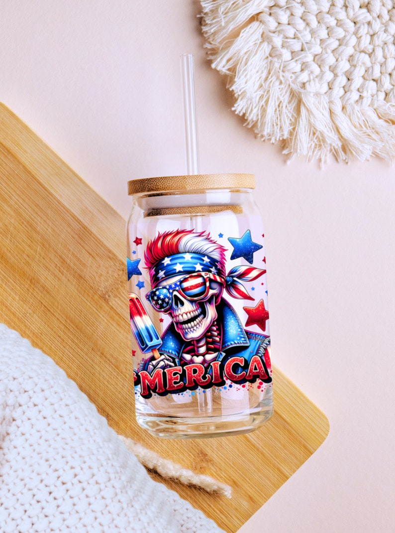 May include: A glass tumbler with a bamboo lid and a straw. The tumbler has a colorful graphic of a skeleton wearing sunglasses and a bandana with the word "MERICA" printed on it.