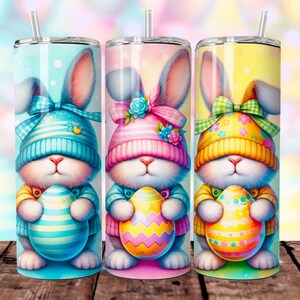 May include: Three Easter-themed stainless steel tumblers with colorful bunny designs. Each bunny is wearing a hat and holding an Easter egg. The tumblers are perfect for spring celebrations.