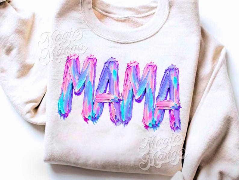 May include: A cream-coloured sweatshirt featuring the word "MAMA" in large, colourful, textured lettering. The letters are painted with shades of pink, blue, and purple, giving a brushstroke effect. The sweatshirt has a crew neck.
