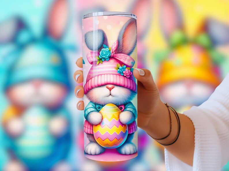 May include: A pink and blue stainless steel tumbler with a cartoon bunny holding a colorful Easter egg. The bunny is wearing a pink and white hat with a blue bow.