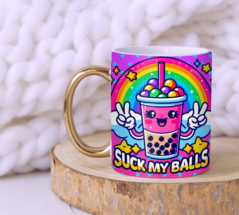 May include: A white ceramic mug with a gold handle features a cartoon illustration of a pink bubble tea cup with a rainbow and stars. The text "SUCK MY BALLS" is printed on the mug.