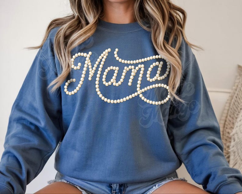 May include: A blue sweatshirt with the word "Mama" in a cursive font, outlined with small, white, pearl-like beads. The sweatshirt has long sleeves and a crew neck.