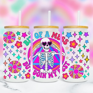 May include: Three white glass tumblers with bamboo lids and straws. Each tumbler features a colorful design with a skeleton wearing heart-shaped sunglasses, a rainbow, and the text "Bit of a mess but doin' my best". The design includes stars and flowers.