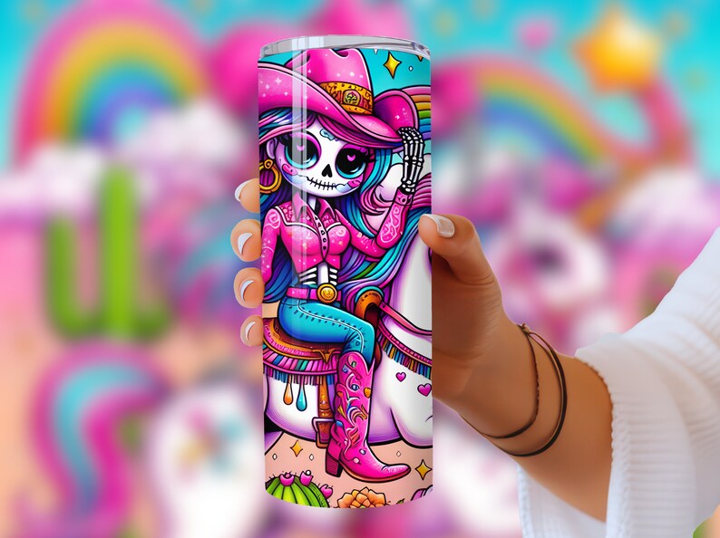 Puede incluir: Un vaso de acero inoxidable rosa y azul con una ilustraci&oacute;n colorida de un esqueleto con un sombrero de vaquero rosa montando un unicornio. El unicornio tiene una crin y una cola de arco&iacute;ris.