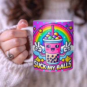 May include: A pink and white ceramic mug with a cartoon image of a boba tea cup with a rainbow and the text "SUCK MY BALLS".