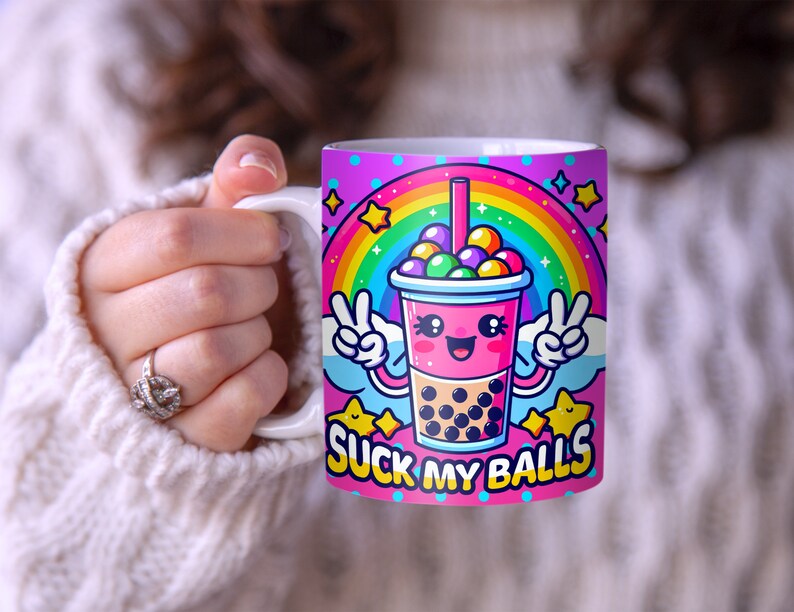 May include: A pink and white ceramic mug with a cartoon image of a boba tea cup with a rainbow and the text "SUCK MY BALLS".