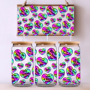 Puede incluir: Un letrero de madera y tres vasos de vidrio con tapas de bamb&uacute;. El letrero y los vasos est&aacute;n decorados con pegatinas en forma de coraz&oacute;n de colores con varias frases. Los vasos son transparentes y tienen forma cil&iacute;ndrica.