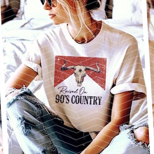 May include: White t-shirt with a red and white graphic of a bull skull and the text "Raised On 90's Country".