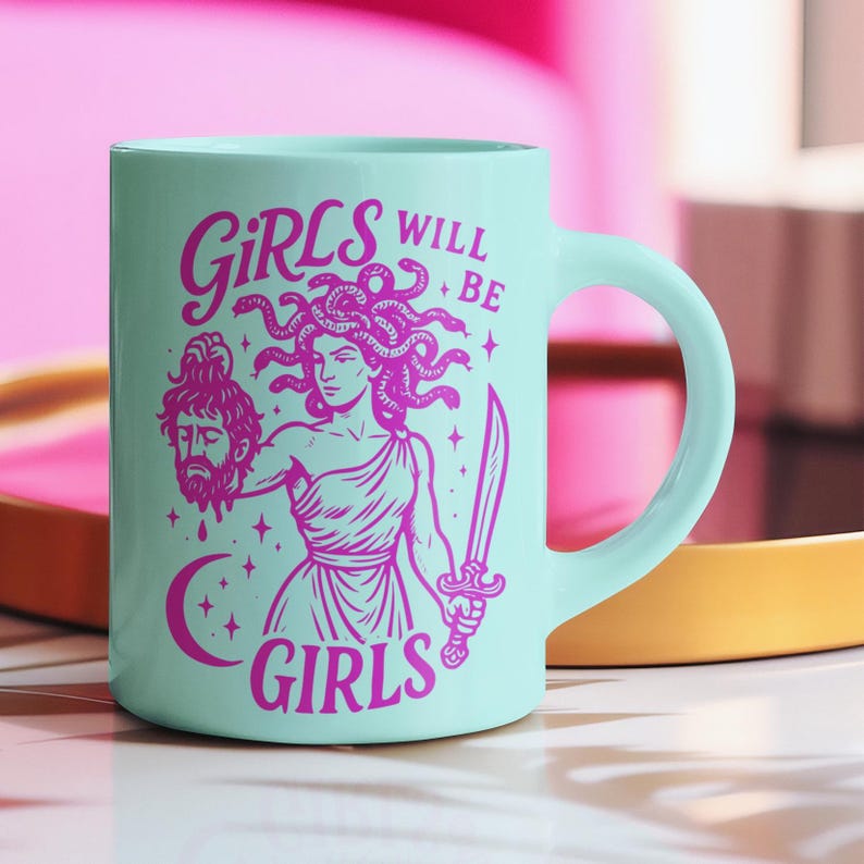 May include: A light teal ceramic mug with a pink illustration of Medusa holding a sword and a severed head. The text "GIRLS WILL BE GIRLS" is printed in pink. The mug has a curved handle.