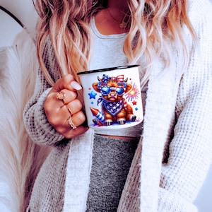 May include: White enamel mug with a black rim and handle. The mug features a cartoon cow wearing a red, white, and blue bandana and sunglasses. The cow is surrounded by stars and fireworks.
