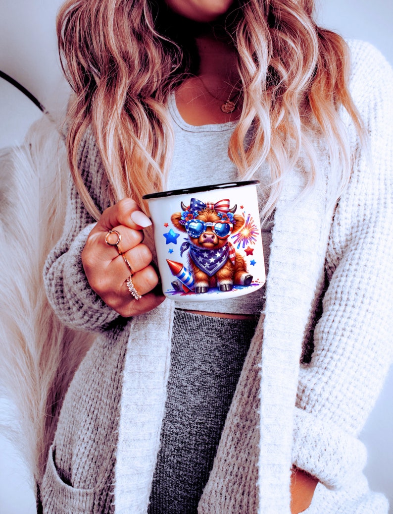 May include: White enamel mug with a black rim and handle. The mug features a cartoon cow wearing a red, white, and blue bandana and sunglasses. The cow is surrounded by stars and fireworks.