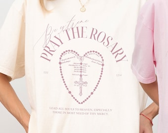 May include: Two oversized t-shirts with a pink rosary design and the text "Pray the Rosary" in a pink script font. The text below the rosary design reads "Lead all souls to heaven, especially those in most need of thy mercy."