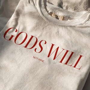 May include: A white t-shirt with the text "GODS WILL NOT MINE" printed in red.