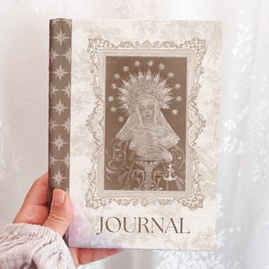 以下が含まれることがあります： 宗教的な人物のセピア色のイラストが施されたジャーナル。装飾的なディテールで縁取られています。表紙には「JOURNAL」の文字。背表紙は星の繰り返し模様で装飾されています。