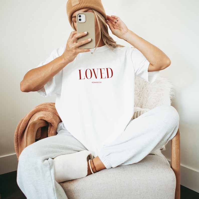 May include: White t-shirt with the word "LOVED" in red lettering and the text "ROMANS 5:8" in smaller red lettering.