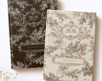 May include: Two hardcover vow books with a toile de jouy pattern. The black book features the text "DEAR Ryan" and "VOWS TO MY HUSBAND." The cream book features the text "DEAR Samantha" and "VOWS TO MY WIFE." Both books have ornate decorative frames.