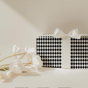 May include: A rectangular gift box wrapped in black and white diamond patterned paper, tied with a white satin ribbon. White flowers are arranged to the left. The words "BIRTHDAYS", "HOLIDAYS", and "WEDDINGS" are below.