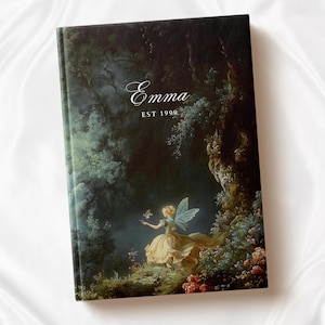 Puede incluir: Una cubierta de diario verde oscuro con una pintura de un hada en un entorno de bosque. El hada lleva un vestido amarillo y tiene alas. El texto "Emma EST 1999" est&aacute; impreso en la cubierta.