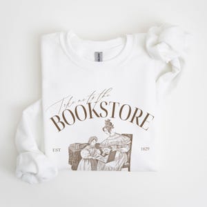 May include: White sweatshirt with brown text that reads "Take me to the Bookstore" with an illustration of two women reading a book. The text also includes "EST 1829".