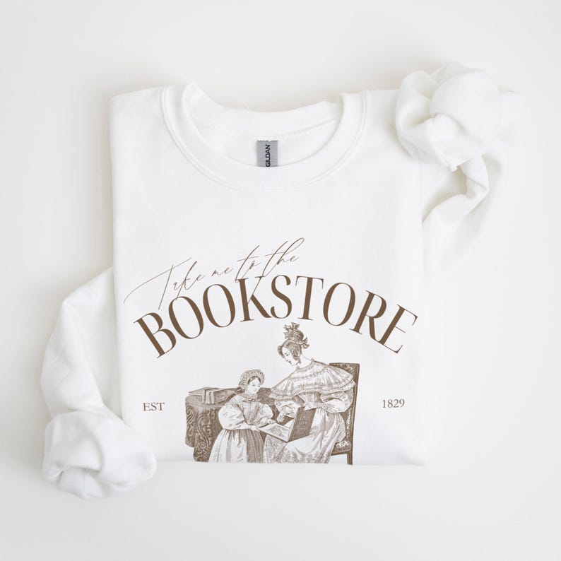 May include: White sweatshirt with brown text that reads "Take me to the Bookstore" with an illustration of two women reading a book. The text also includes "EST 1829".