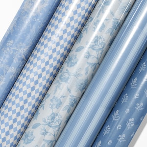May include: A collection of rolled wrapping paper in various patterns. Designs include floral, diamond, and striped patterns in shades of blue and white. The paper has a glossy finish.