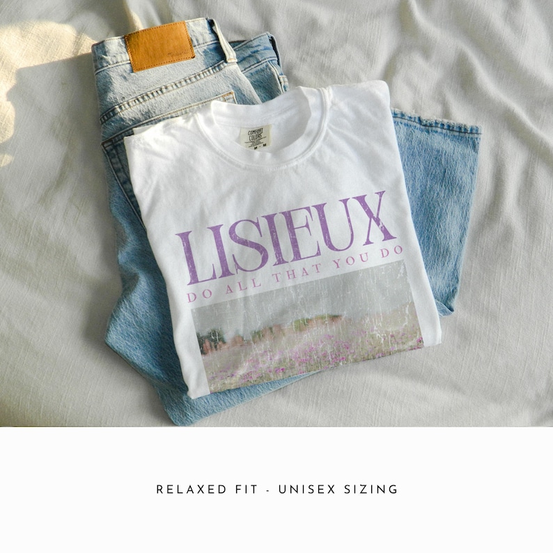May include: A white t-shirt with the word "LISIEUX" in purple, and the phrase "DO ALL THAT YOU DO" below a landscape image. The shirt is paired with light blue denim jeans. The items are arranged on a white surface.