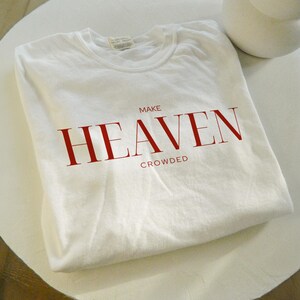 Op de afbeelding: Wit T-shirt met rode tekst die "MAKE HEAVEN CROWDED" luidt.