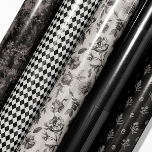 May include: Assortment of rolled wrapping paper with various patterns. Designs include a black and white checkerboard, floral, and botanical prints. The paper is in shades of black, white, and gray, creating a monochromatic aesthetic. Ideal for gifts and crafts.