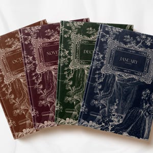 Op de afbeelding: Vier hardcover dagboeken met decoratieve bloemmotieven en gouden letters. De dagboeken zijn gelabeld met "Oktober", "November", "December" en "Januari".