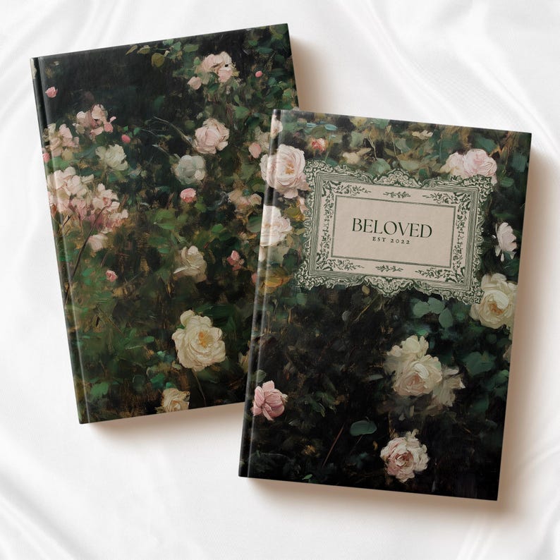 K&ouml;nnte beinhalten: Zwei Hardcover-Journale mit einem floralen Design mit rosa Rosen und gr&uuml;nen Bl&auml;ttern. Der Einband eines Journals tr&auml;gt den Text "BELOVED EST 2023" in einem dekorativen Rahmen.