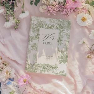 May include: A white book with a green floral design and the text "Her Vows" in cursive. The book has the names "Noah & Emma" and the date "02.26.21" printed on the front.