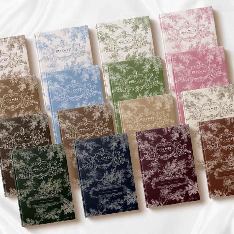 May include: A collection of rectangular hardcover journals featuring a toile de jouy pattern in various colors including blue, green, pink, brown, and dark red. Each journal cover displays the text BELOVED in a decorative frame at the top.