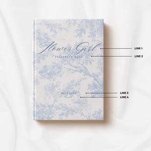 May include: A hardcover book with a light blue and white toile pattern featuring tree motifs. The cover text reads Flower Girl, ELIZABETH ROSE, WITH LOVE, and 2026, with black lines pointing to each line of text for customization reference.