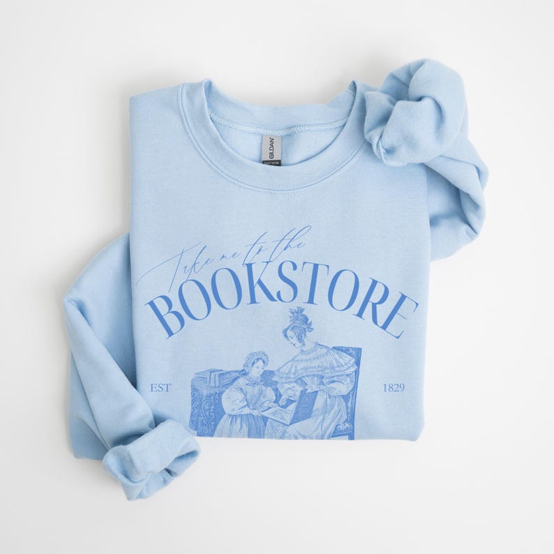 May include: Light blue sweatshirt with the text "Take me to the Bookstore" in blue lettering. The sweatshirt features a vintage illustration of two women in a bookstore.