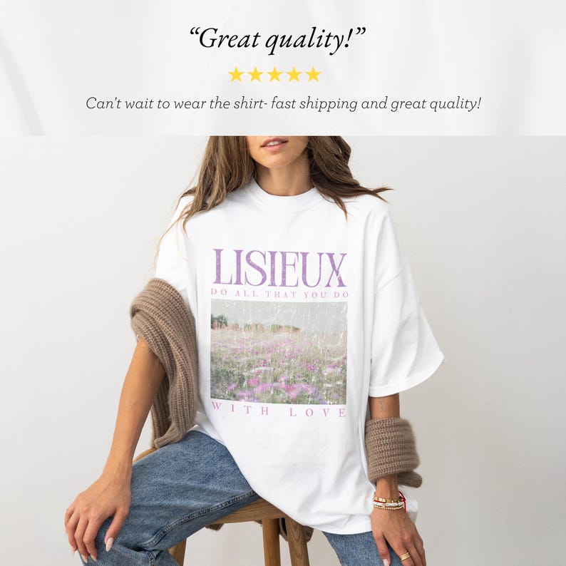 May include: White t-shirt with the word "LISIEUX" in purple, along with the text "DO ALL THAT YOU DO WITH LOVE." The shirt features a landscape image with purple flowers. The shirt is worn by a person.