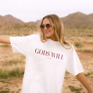 May include: White t-shirt with the text "GODS WILL NOT MINE" printed in red.