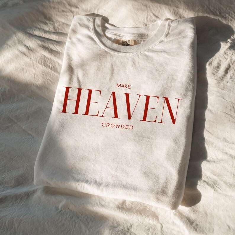 Op de afbeelding: Wit T-shirt met rode tekst die "MAKE HEAVEN CROWDED" luidt.