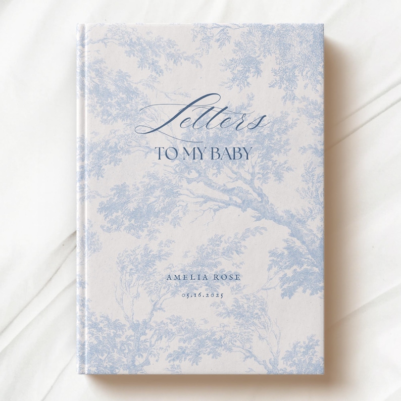 May include: A white book with a blue floral pattern and the text "Letters to My Baby" on the front cover. The book also includes the name "Amelia Rose" and the date "05.16.2025".