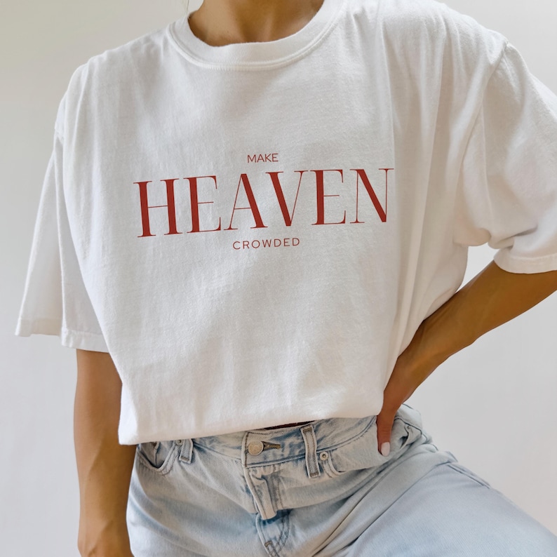 Op de afbeelding: Wit oversized T-shirt met de tekst "MAKE HEAVEN CROWDED" in rood gedrukt.