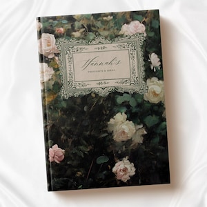 K&ouml;nnte beinhalten: Ein dunkelgr&uuml;nes Journal mit einem floralen Design mit wei&szlig;en und rosa Rosen. Der Umschlag hat einen dekorativen Rahmen mit dem Text "Hannah's Thoughts & Ideas".