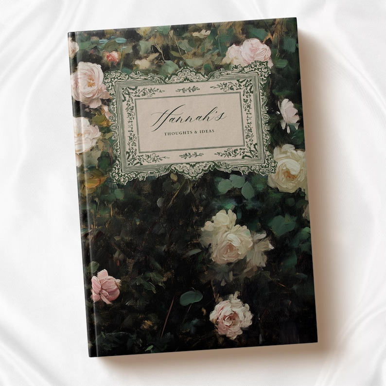 K&ouml;nnte beinhalten: Ein dunkelgr&uuml;nes Journal mit einem floralen Design mit wei&szlig;en und rosa Rosen. Der Umschlag hat einen dekorativen Rahmen mit dem Text "Hannah's Thoughts & Ideas".
