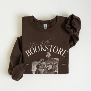 May include: Brown sweatshirt with a white graphic that says "Take me to the bookstore" with an illustration of two women reading a book. The text "EST 1829" is also included in the graphic.