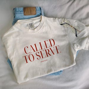 May include: A white t-shirt with the words "Called to Serve" in red lettering and the scripture reference "Mark 10:45" underneath.
