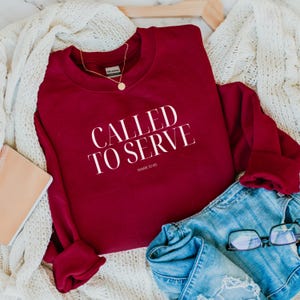 May include: A maroon sweatshirt with the text "CALLED TO SERVE" in white lettering and the scripture reference "MARK 10:45" in smaller white lettering.