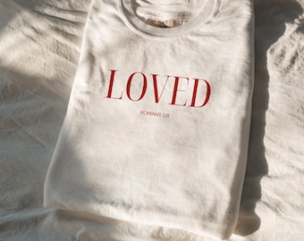 May include: White t-shirt with the word "LOVED" in red lettering and the text "ROMANS 5:8" underneath.