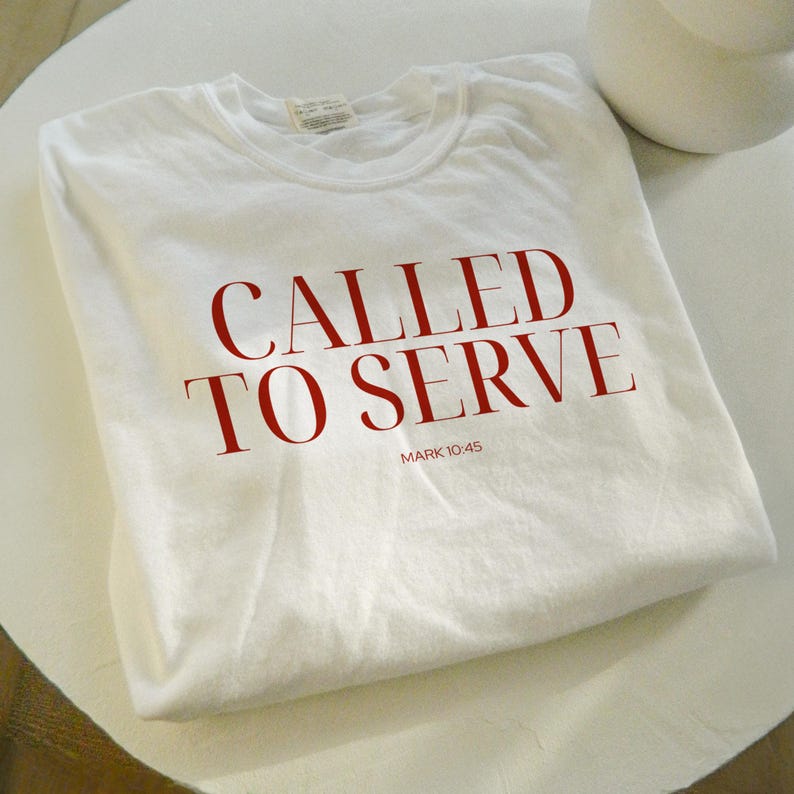 May include: White t-shirt with the text "CALLED TO SERVE" in red lettering and the scripture reference "MARK 10:45" in smaller red lettering.