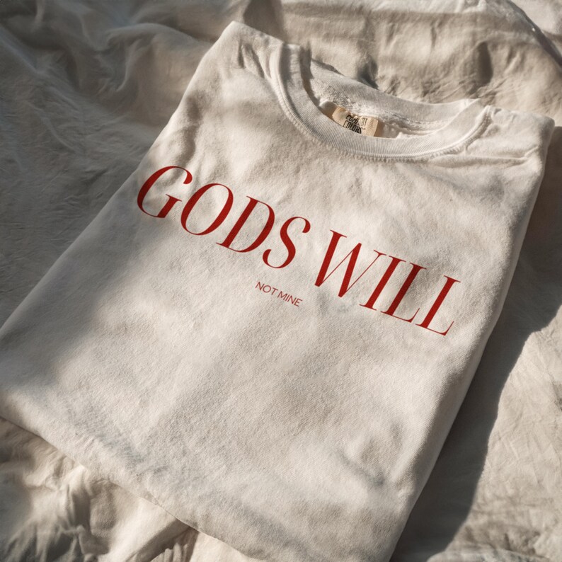 May include: A white t-shirt with the text "GODS WILL NOT MINE" printed in red.